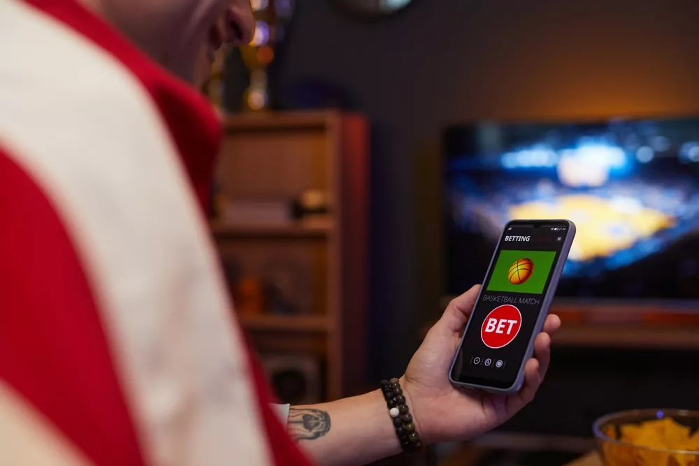 Smartphone mit Wettschein vor einem Basketballspiel im Fernsehen